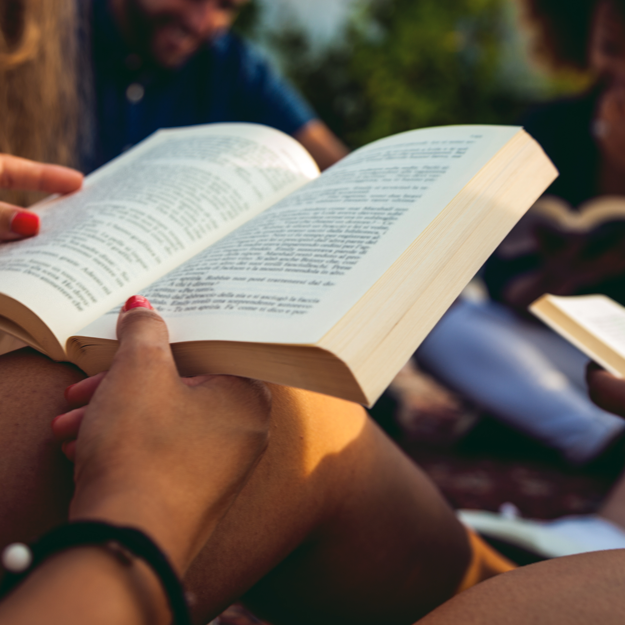 closeup of a book, held by a woman reading outside with a group 