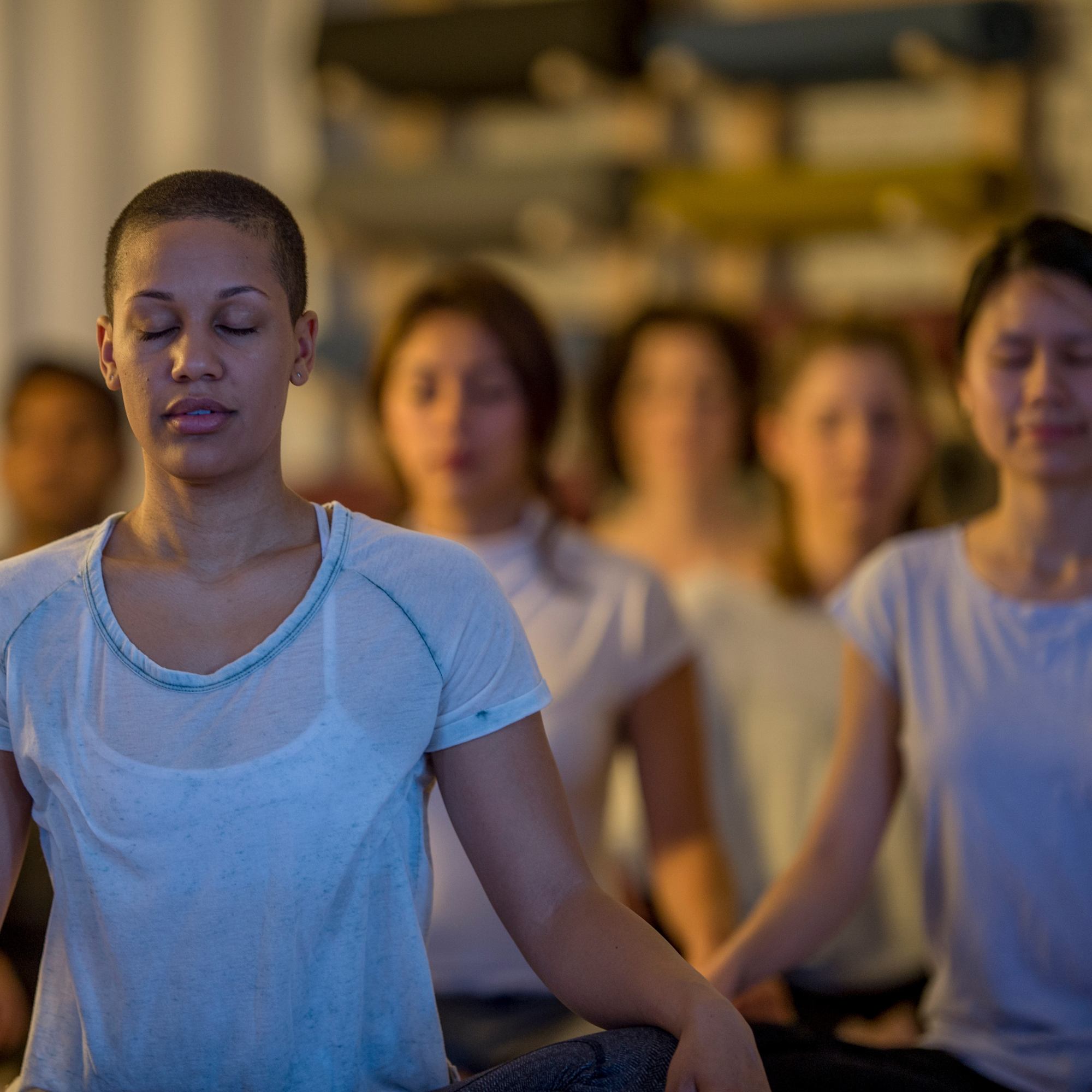 group of meditators sitting in lotus position on the floor with a woman in the foreground