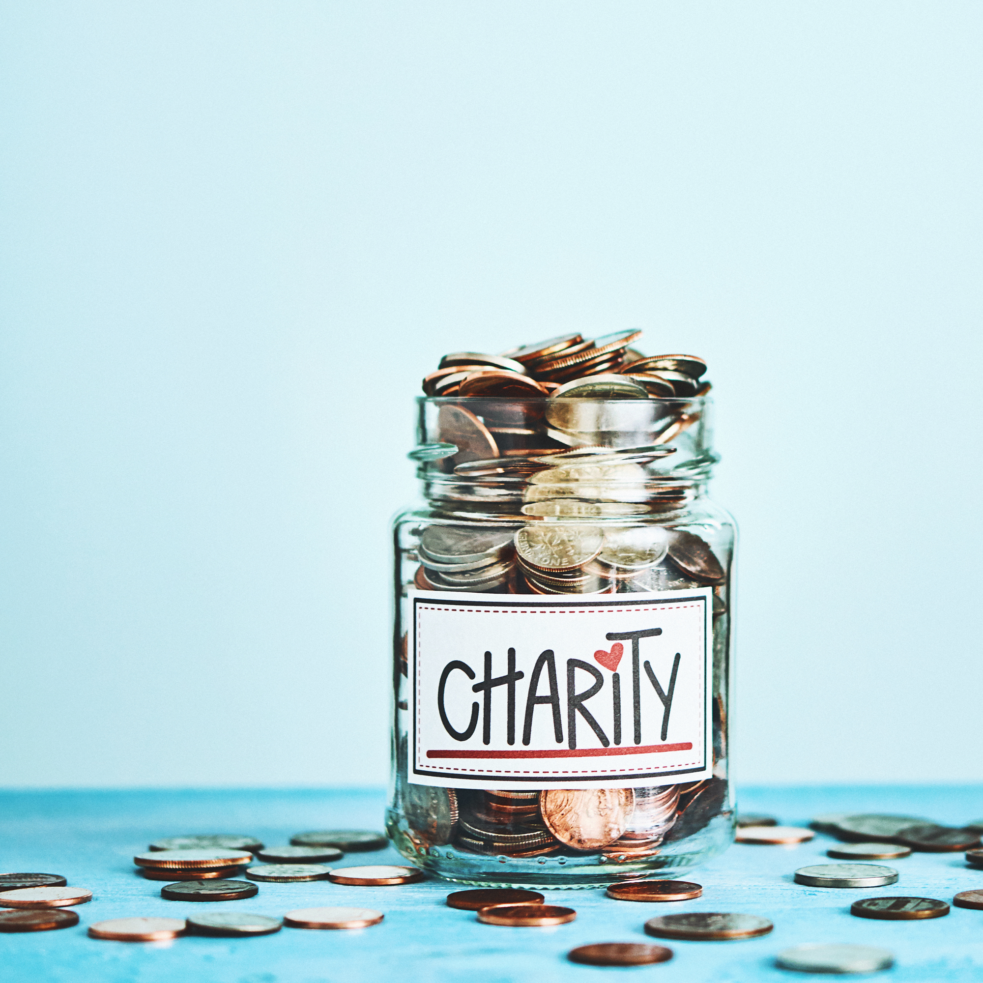 photo of a jar labeled "charity" that is overflowing with coins spilling out