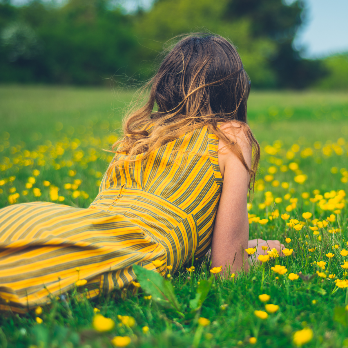 Photo of a woman wearing a yellow dress lying in a field of small yellow flowers.