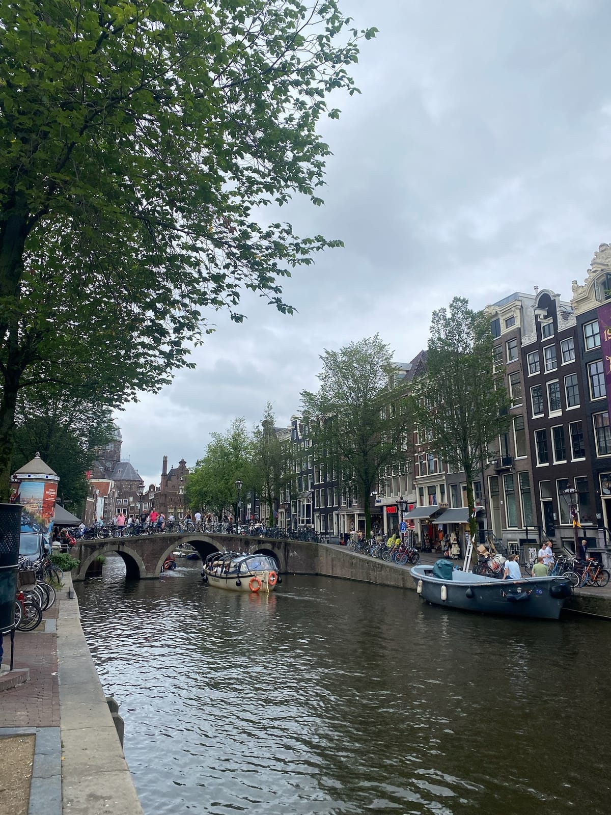 A photo of a canal in Amsterdam, Netherlands featuring several small boats, bicycles and colorful row houses.