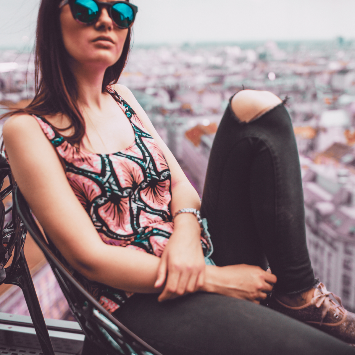 Photo of a woman wearing sunglasses sitting on a balcony overlooking a city.