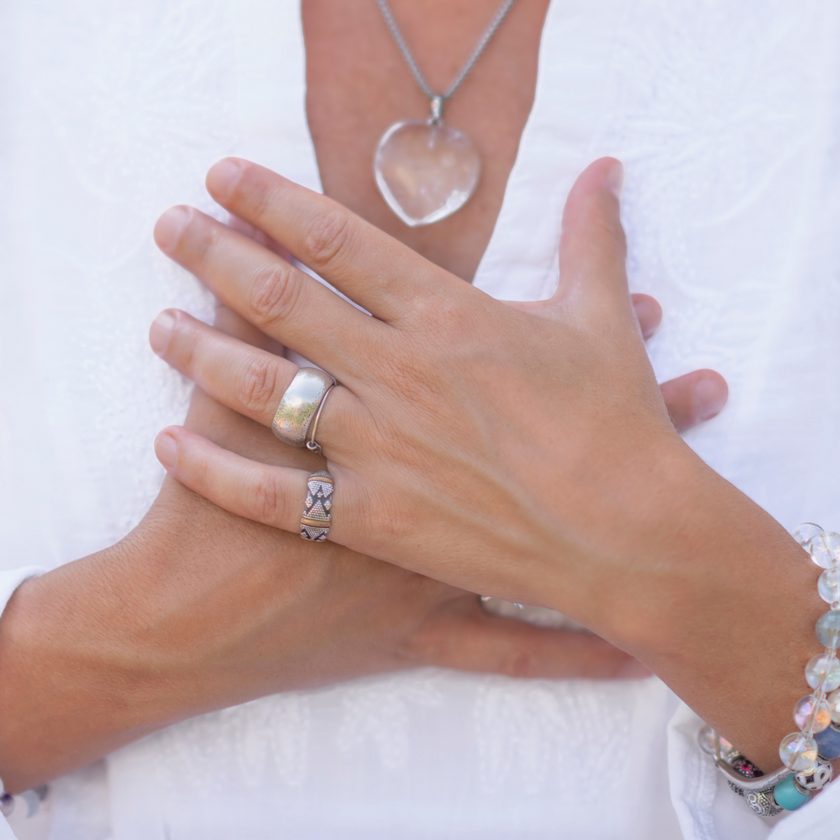 closeup photo of a woman wearing several silver rings holding her hands against her chest