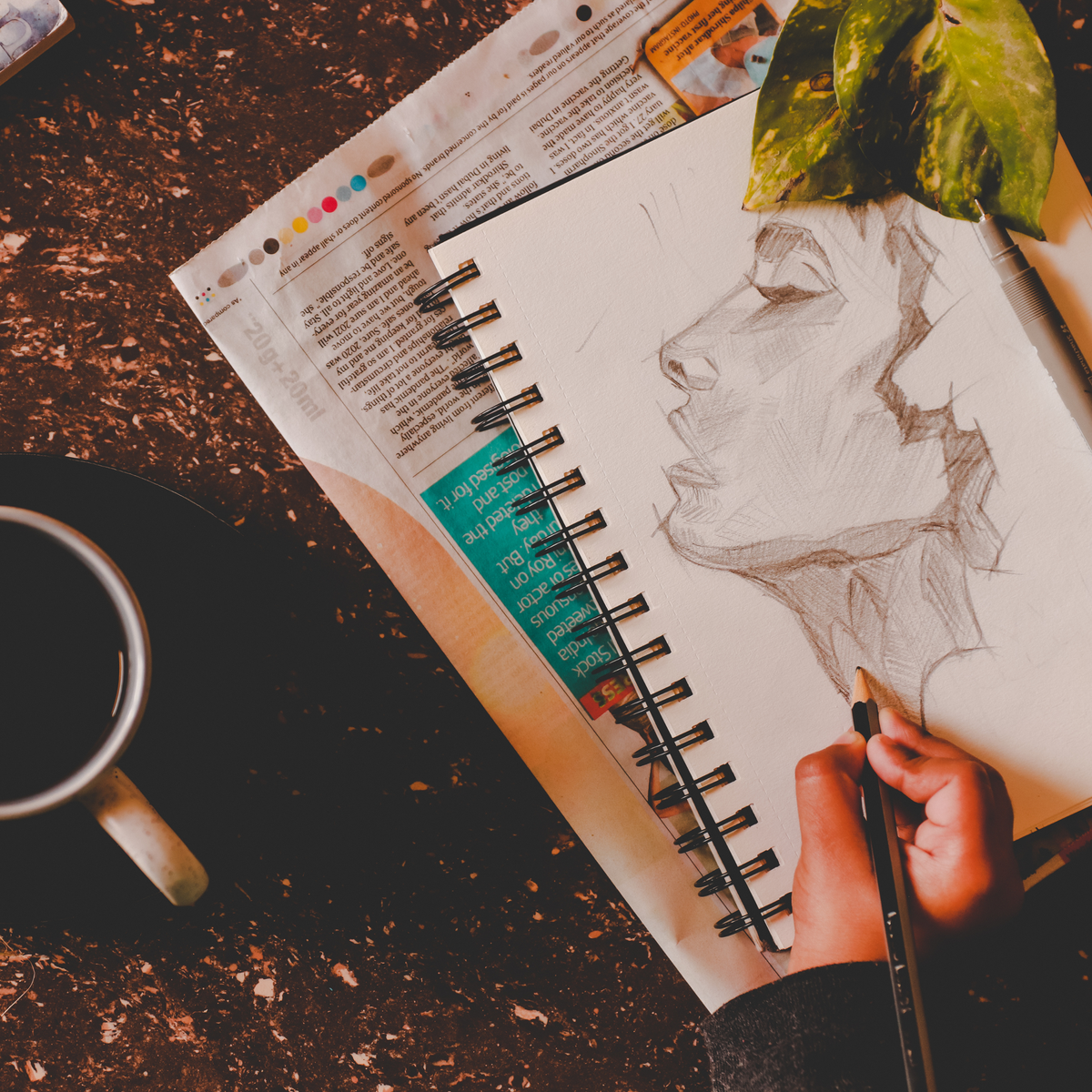 photo of a person sketching the profile of a woman's face with a cup of coffee beside them