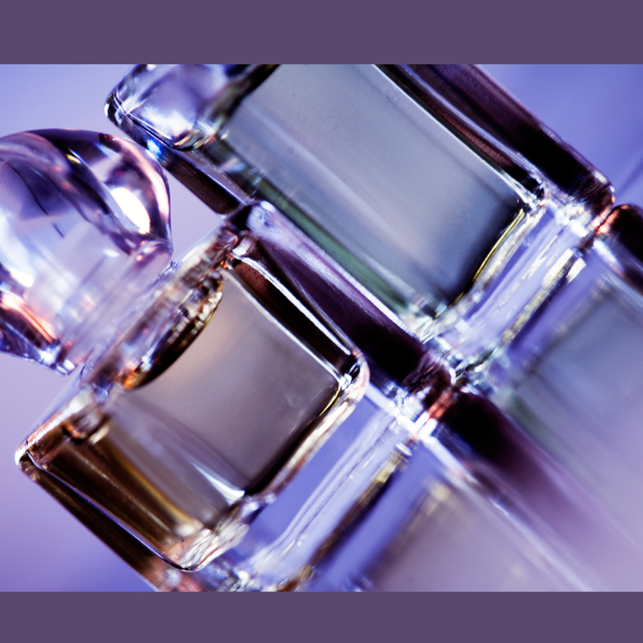 Up close and angled photo of two purple hued glass perfume bottles.