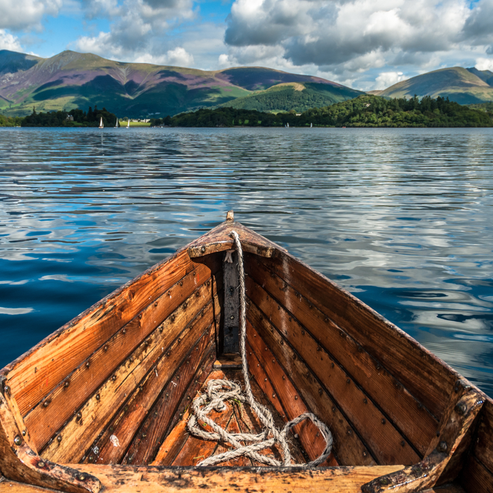 Photo of the bow of boat floating through a lake with mountains in the distance.